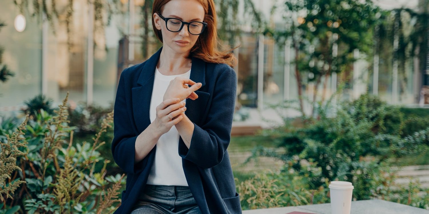 A woman in glasses is sitting on a bench and using her phone. A woman in glasses is sitting on a bench and using her phone.