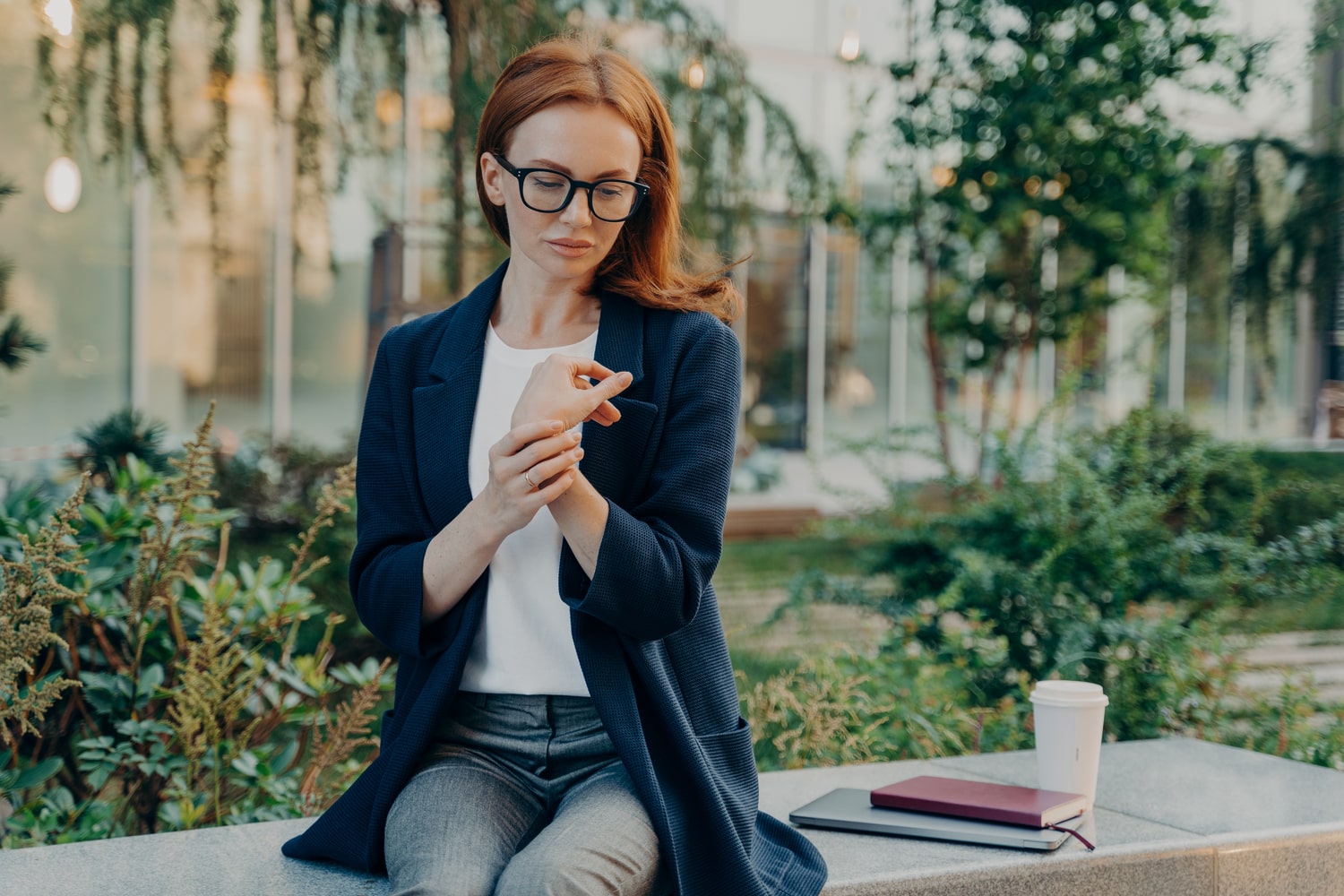 A woman in glasses is sitting on a bench and using her phone.