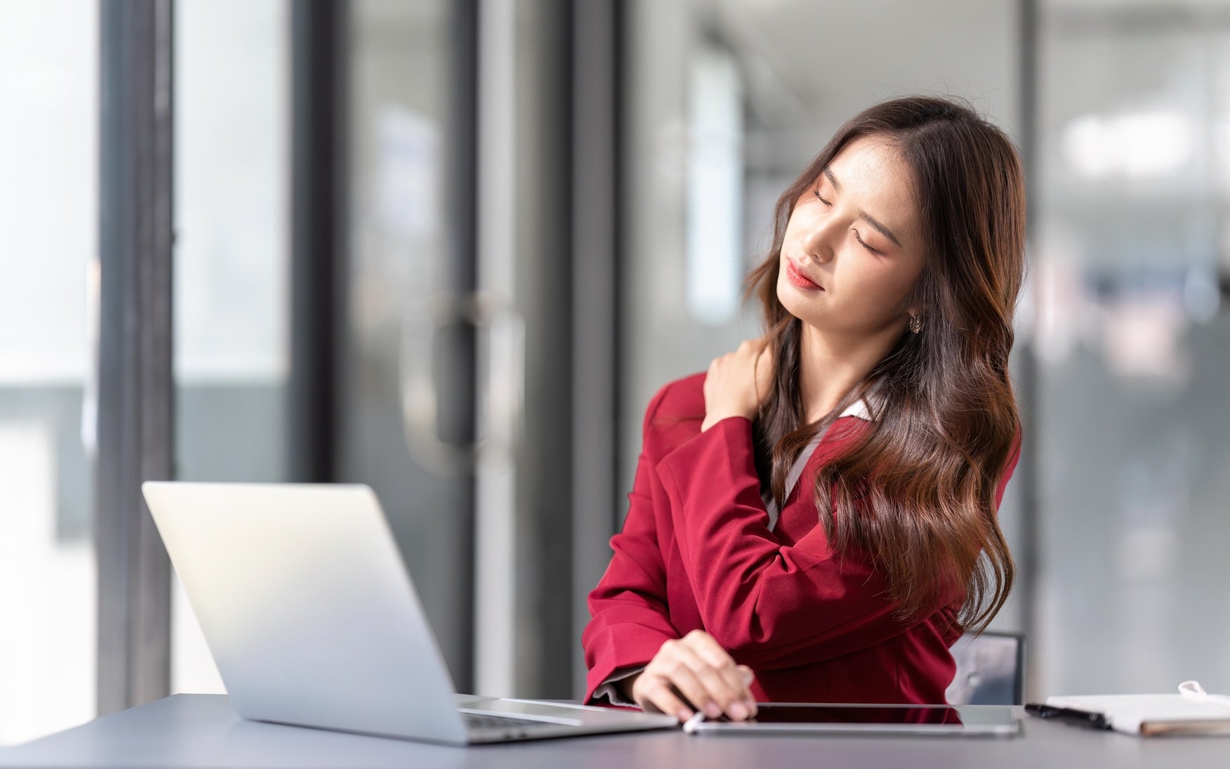 A woman is sitting at a desk with her neck hurting.