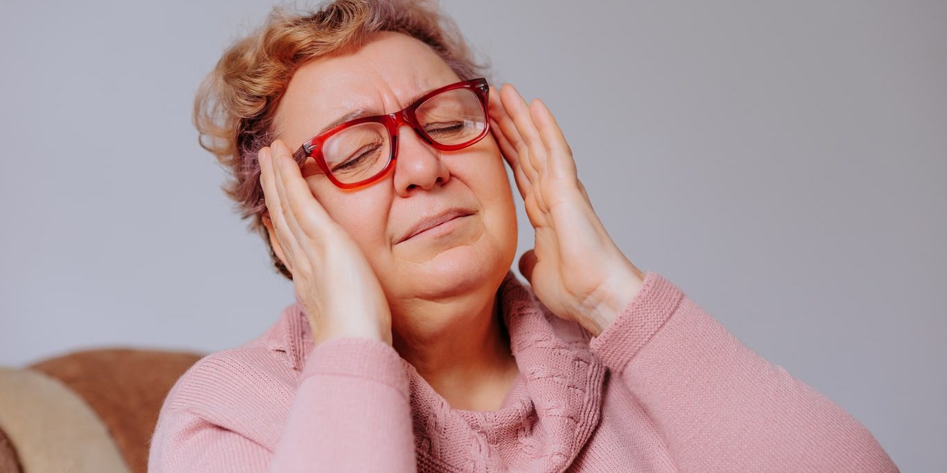 A woman with glasses is holding her hands to her head. A woman with glasses is holding her hands to her head.