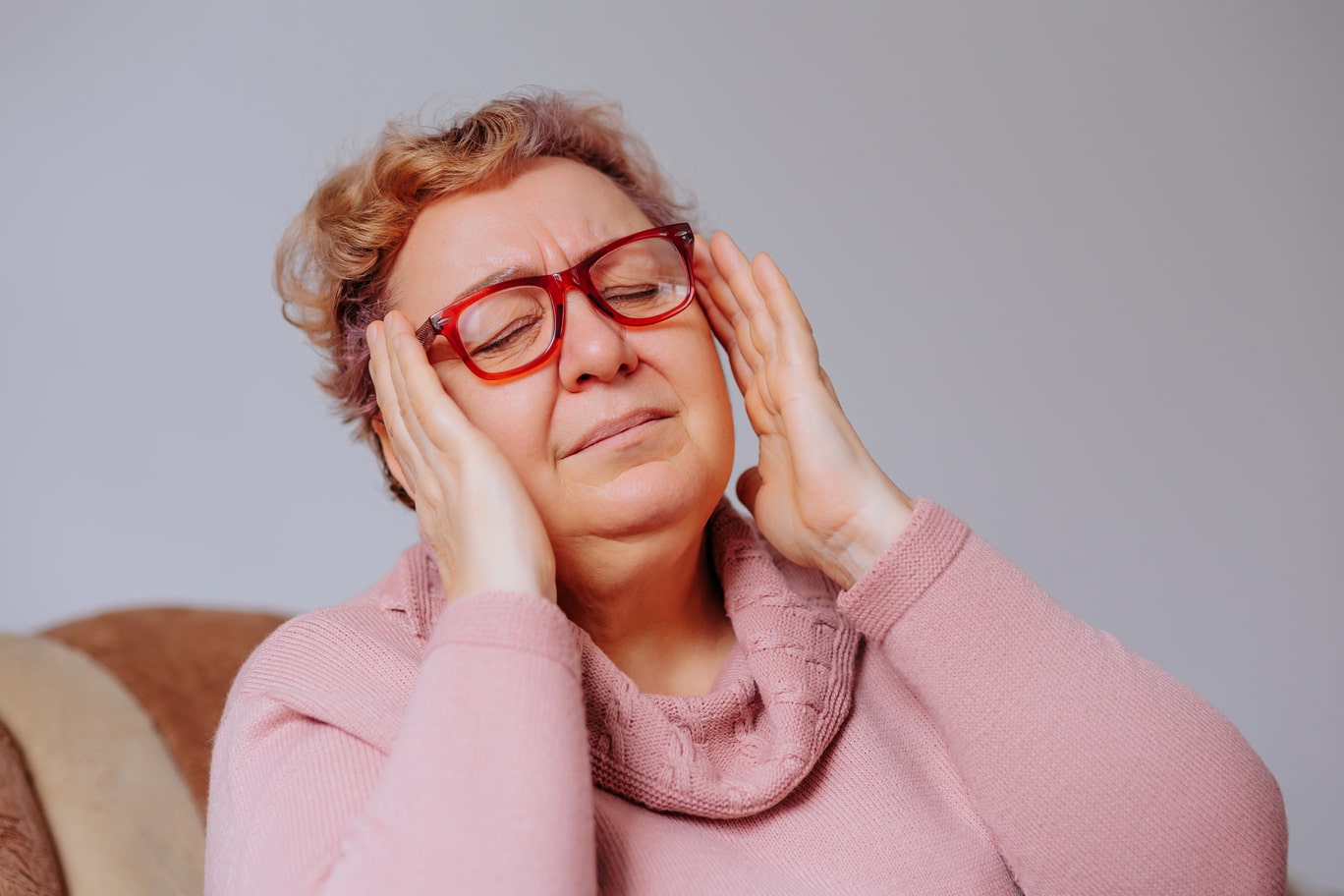 A woman with glasses is holding her hands to her head.