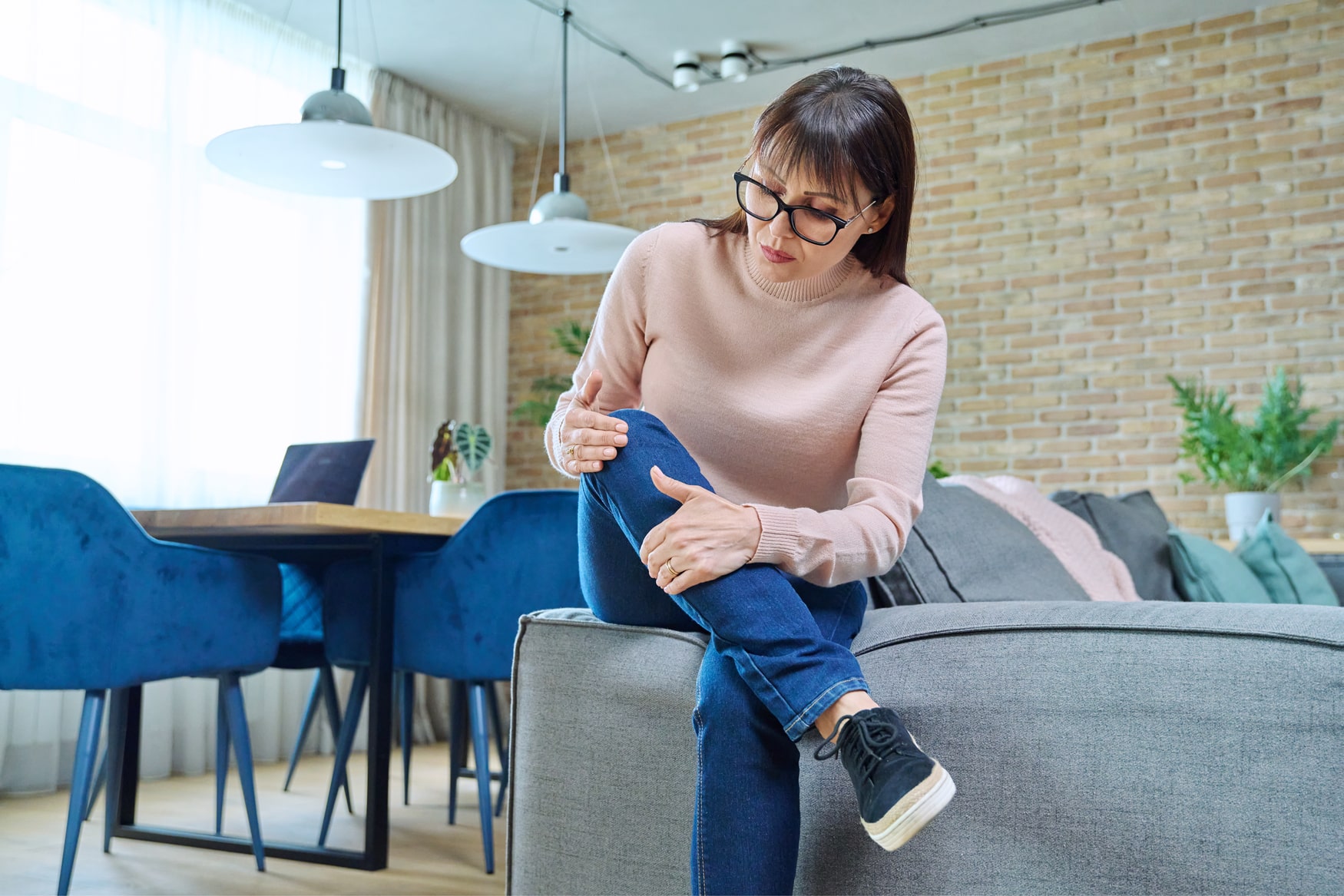 A woman is sitting on a couch with her leg in pain.