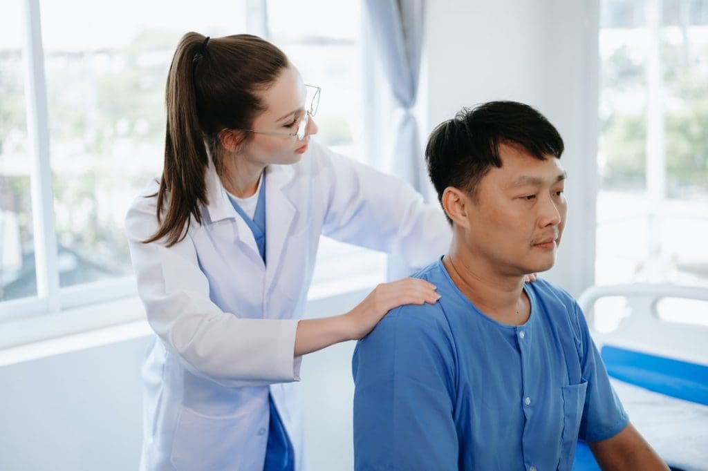 Female physiotherapist in lab coat examining the back of a male patient seated in a clinic. Female physiotherapist in lab coat examining the back of a male patient seated in a clinic.