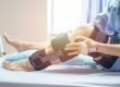 A person with a hospital gown and IV in their hand rests in bed while wearing a large knee brace on one leg. Pain Management for Post-Surgical Recovery