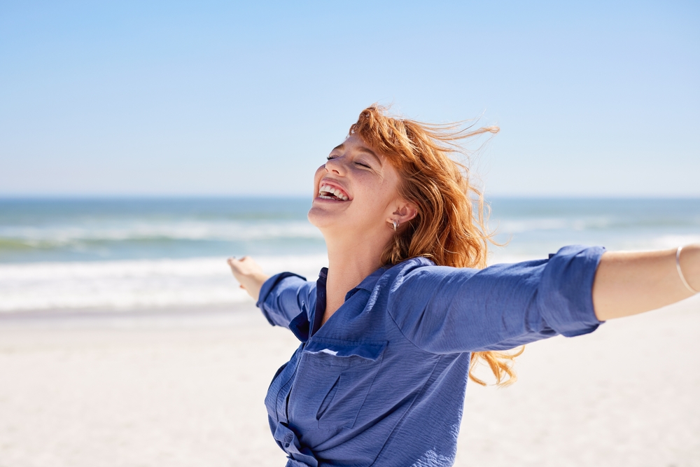 A woman with red hair smiles with outstretched arms on a sandy beach with the ocean and blue sky in the background. A woman with red hair smiles with outstretched arms on a sandy beach with the ocean and blue sky in the background. Chronic Joint Pain