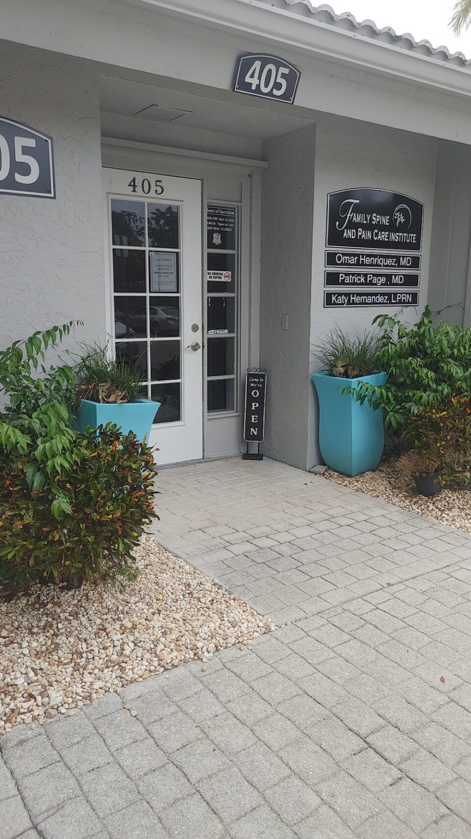 Entrance of the Family Spine and Pain Care Institute at suite 405 with a glass door, “Open” sign, and two large blue planters with greenery on either side. Entrance of the Family Spine and Pain Care Institute at suite 405 with a glass door, "Open" sign, and two large blue planters with greenery on either side. Office to have a procedure such as spinal cord stimulation in venice.
