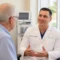 A doctor in a white coat talks to an older male patient in a medical office with palm trees visible outside the window. Discussing the use of Botox for Chronic Migraines.