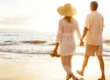 A couple walks hand in hand along a sandy beach at sunset, with gentle waves in the background. An older couple walks hand-in-hand along the shoreline at sunset, symbolizing spinal stenosis pain relief and renewed quality of life.