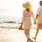 A couple walks hand in hand along a sandy beach at sunset, with gentle waves in the background. An older couple walks hand-in-hand along the shoreline at sunset, symbolizing spinal stenosis pain relief and renewed quality of life.