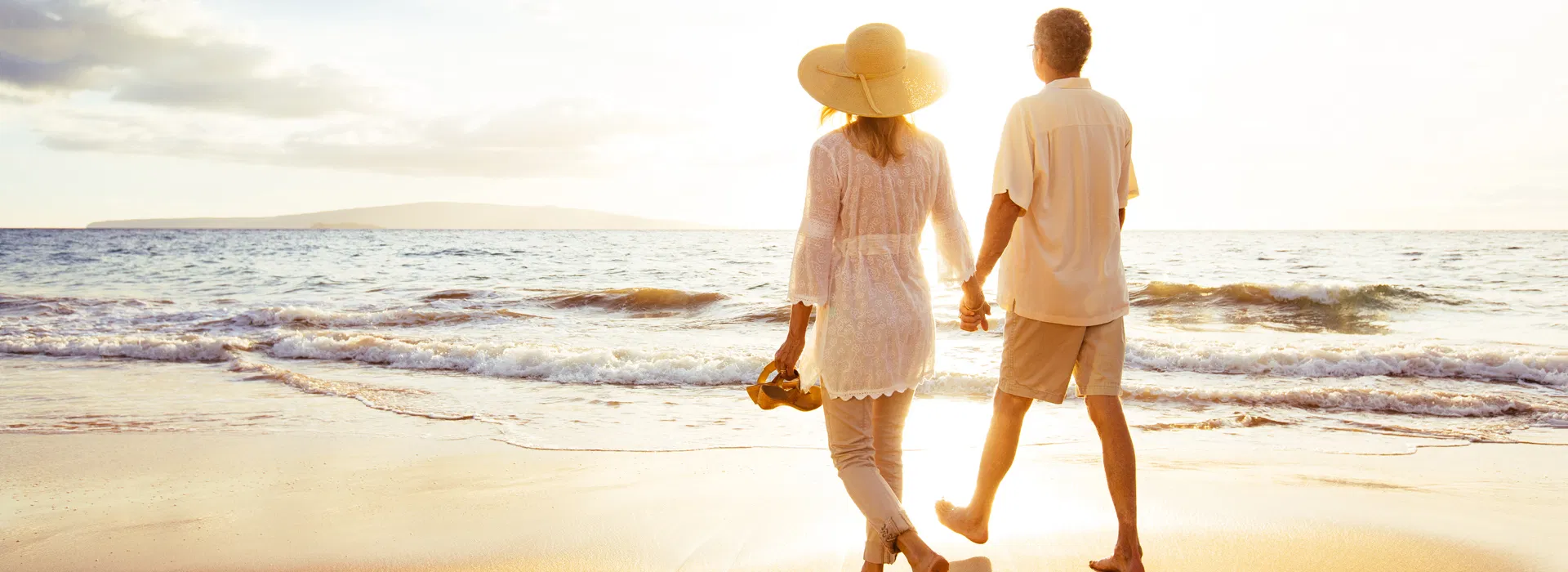 A couple walks hand in hand along a sandy beach at sunset, with gentle waves in the background. An older couple walks hand-in-hand along the shoreline at sunset, symbolizing spinal stenosis pain relief and renewed quality of life.